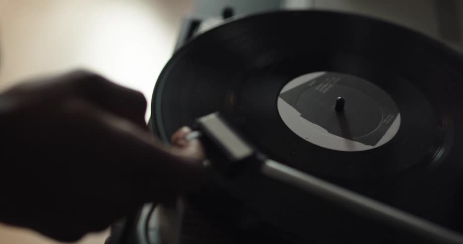 A person places a vinyl record on a record player and positions the needle