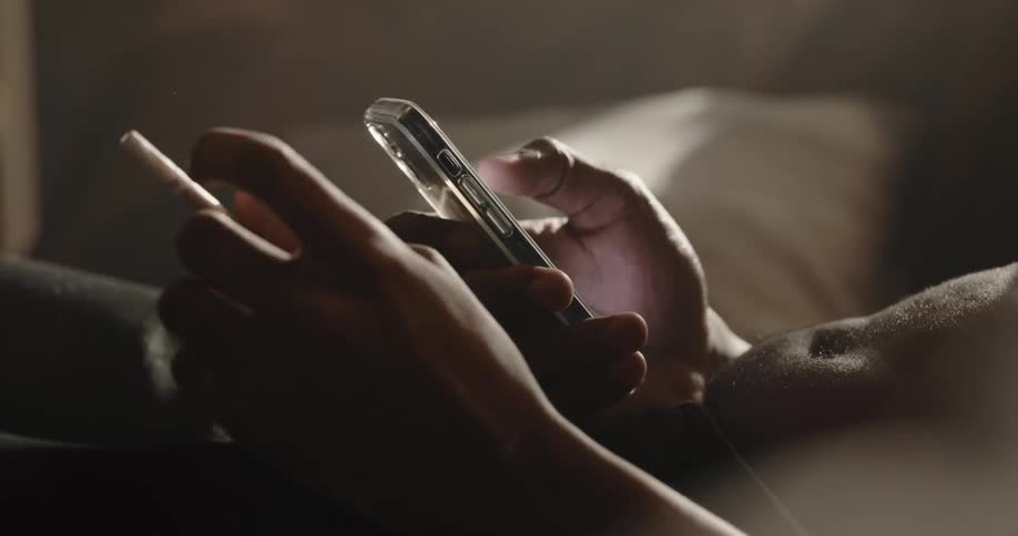 Man scrolls on his cellphone with his thumb while twirling a wrapped candy with his fingers of the other hand