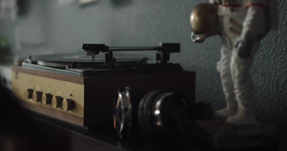 Man turns on record player and picks up camera sitting near statue of astronaut