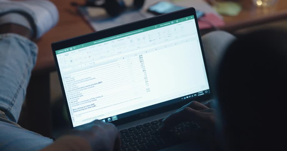 Man with jeans and white shoes works on laptop in living room at home