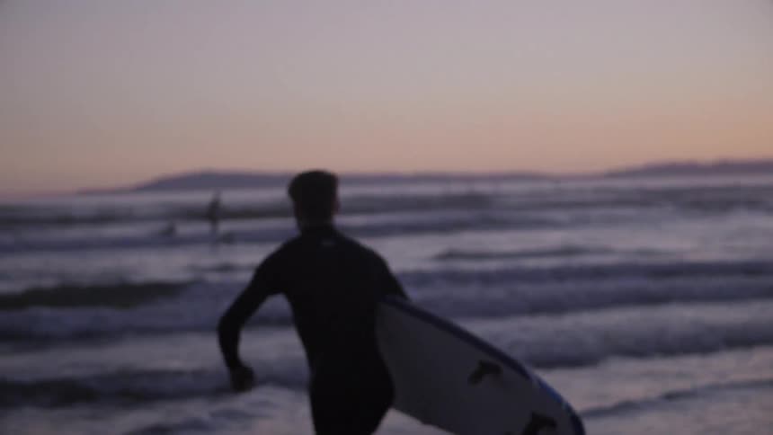 A man holds a surfboard and runs into the water
