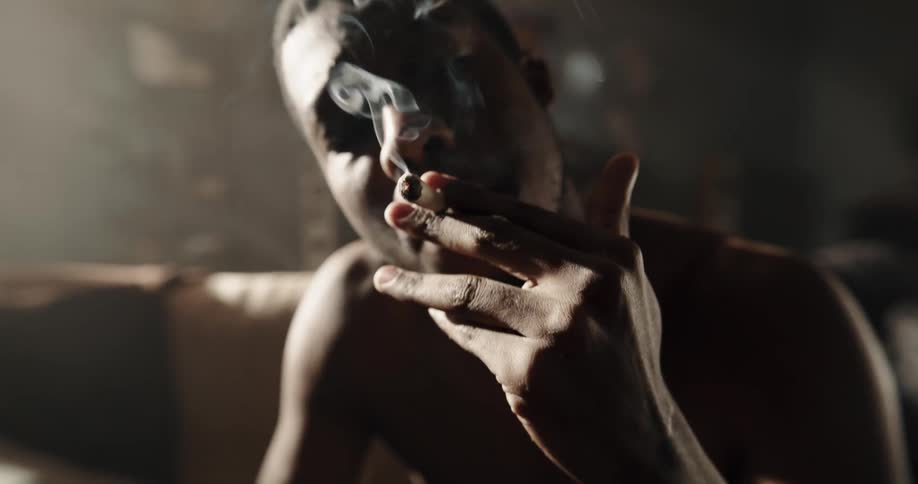 Man lights marijuana roll with a lighter while sitting on couch