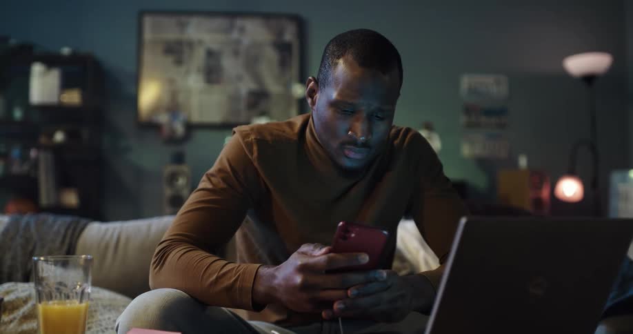 Man sits on couch working with smartphone and laptop