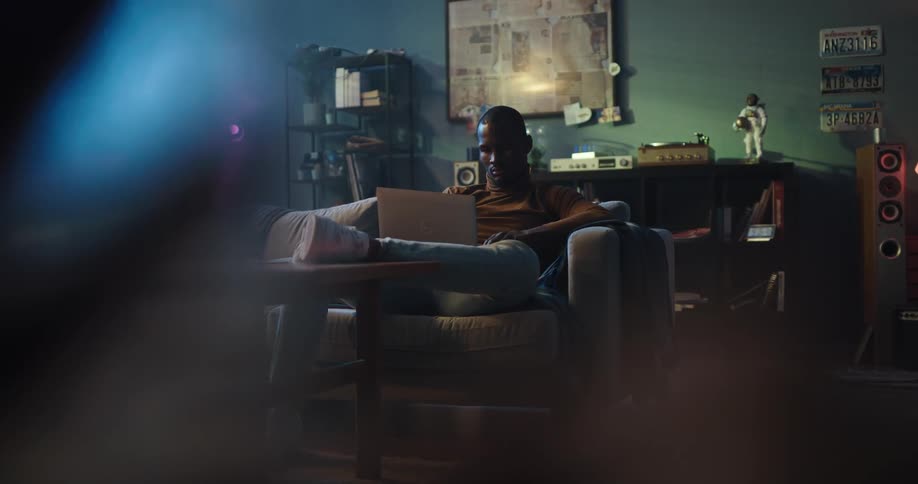 Man sitting in a dark living room on a couch working on his laptop