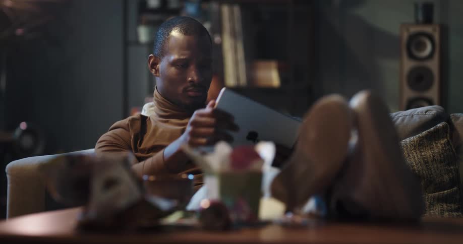 A man plays a game on a computer tablet while sitting on a sofa indoors