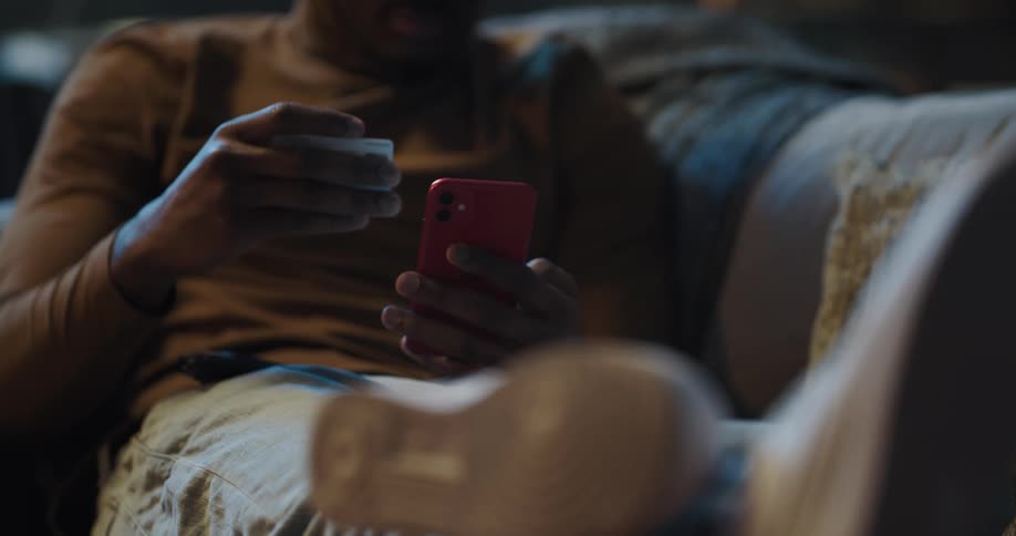 A man is texting on his cell phone while sitting on a couch