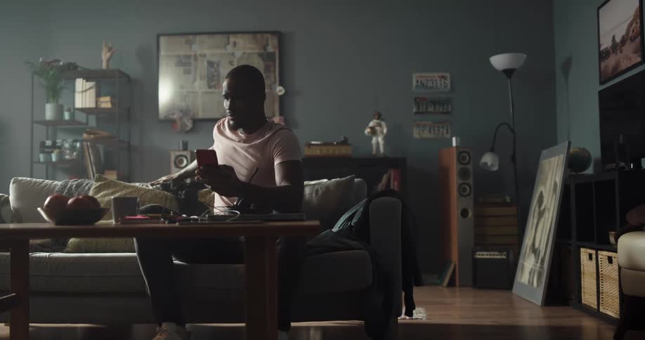Man sitting on a couch looking at his phone in the living room stands up and walks away