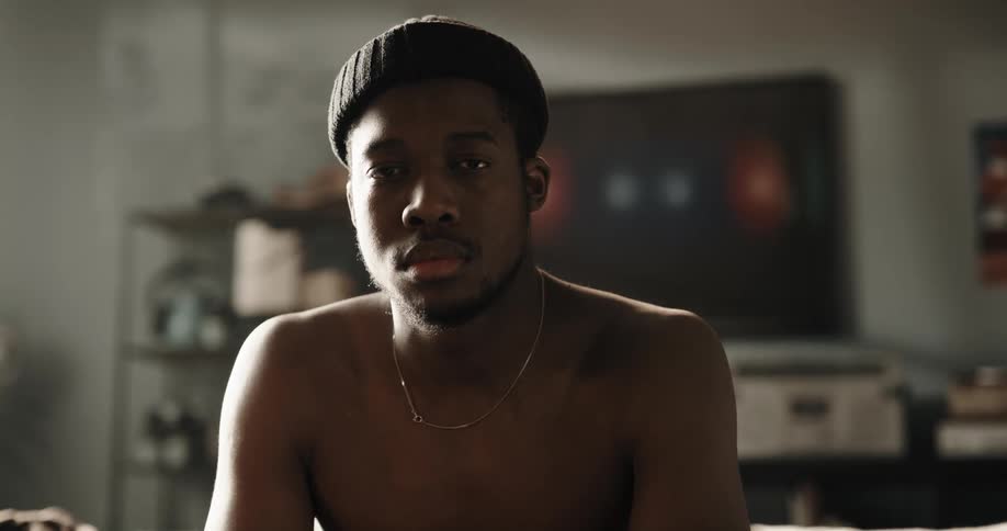Black man wearing a beanie hat and a necklace sitting on the couch indoors