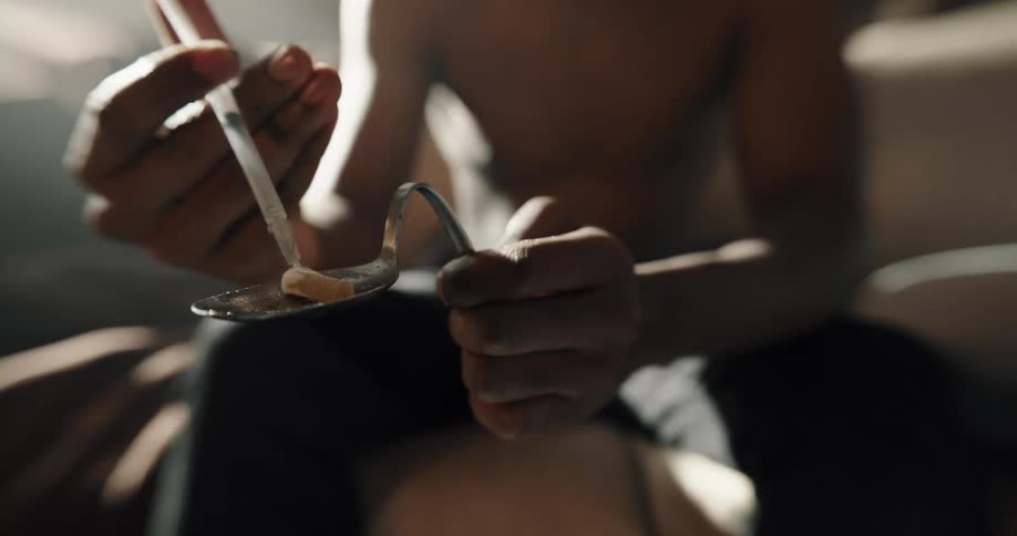 A man sits on a bed and puts drugs in to a syringe