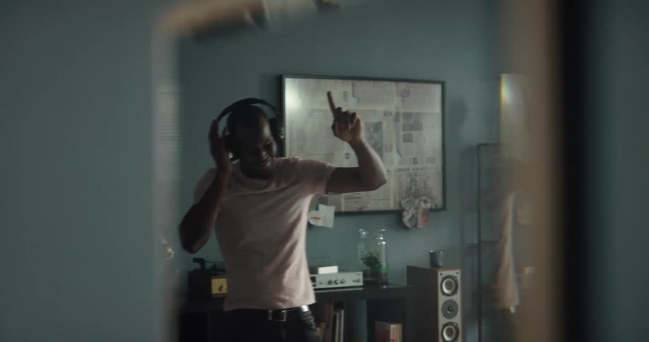 Mirror reflection of a man wearing a headphone listening to some music and dancing in his living room