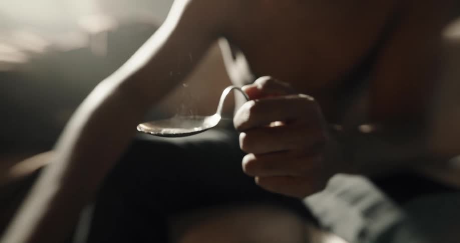 Man sitting on a couch at home uses a syringe to fill a bent spoon to cook drugs