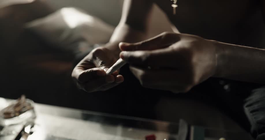 Man with a cross on a chain around his neck licks cigarette paper and rolls it