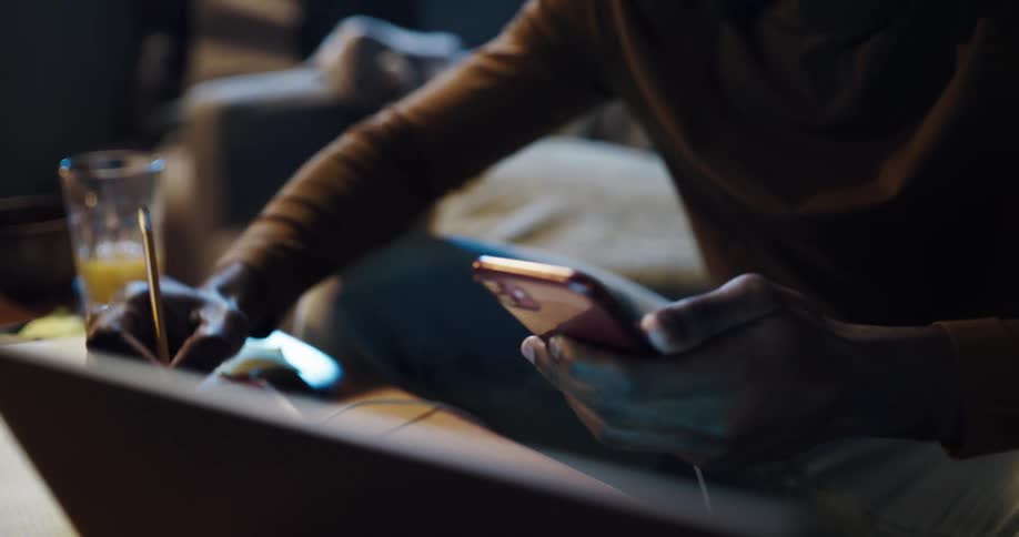 Man sitting on the couch using his smartphone laptop and writing down on a notebook
