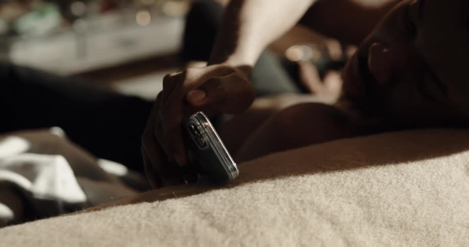 A man uses a smartphone while resting on a sofa indoors during the day