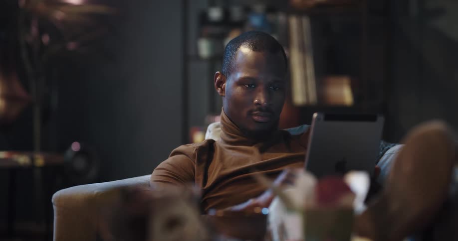 Black man sitting on the couch with his legs up in the center table using his ipad