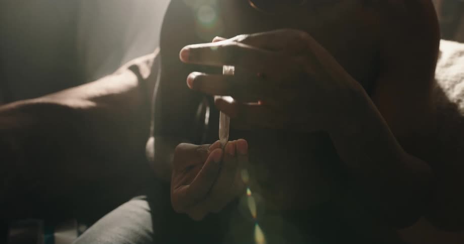 Shirtless black man sitting on the couch rolling a joint