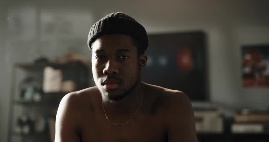 A shirtless man sitting on a couch lifts his head staring at first and then smiling