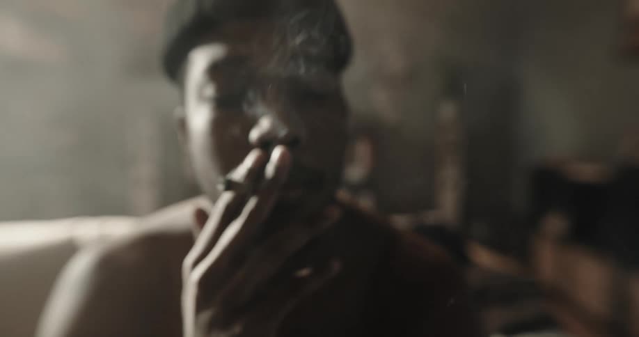 Young man laying in the couch at home smokes a cigarette watching the smoke rise at morning