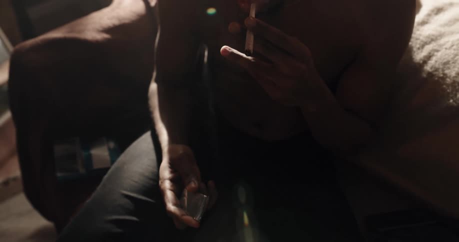 Shirtless black man wearing a beanie hat sitting on the couch smoking a cigarette in the living room