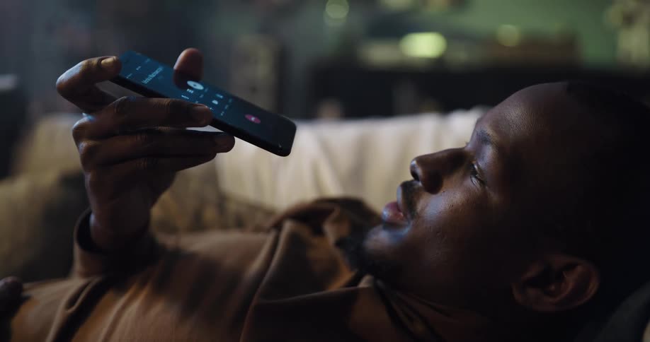Black man lying on the couch talking to someone on his phone
