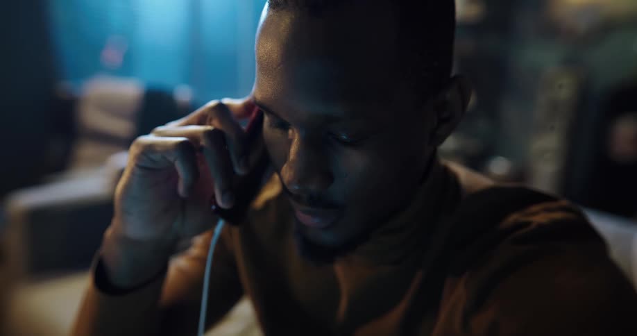 A black man is sitting down talking on his phone