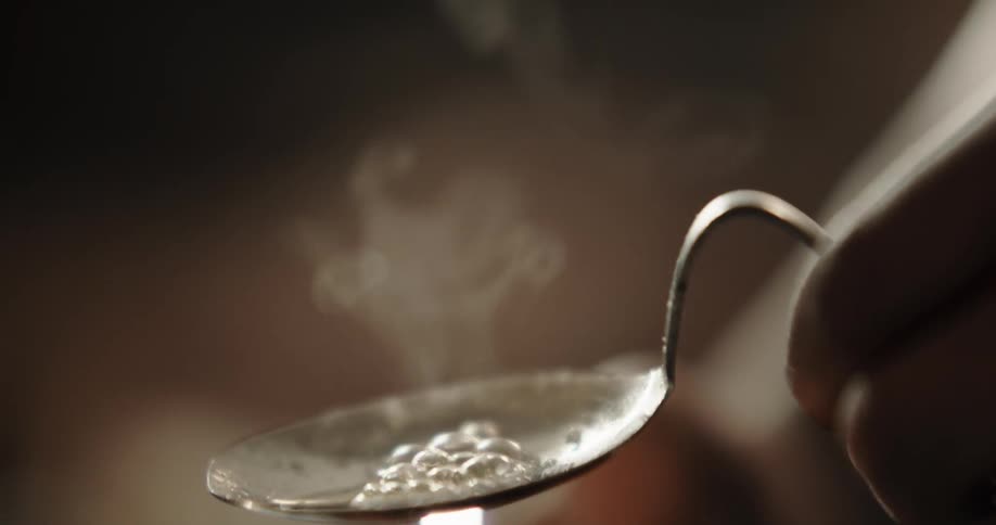 Flames from a lighter heat a substance in a spoon causing bubbles