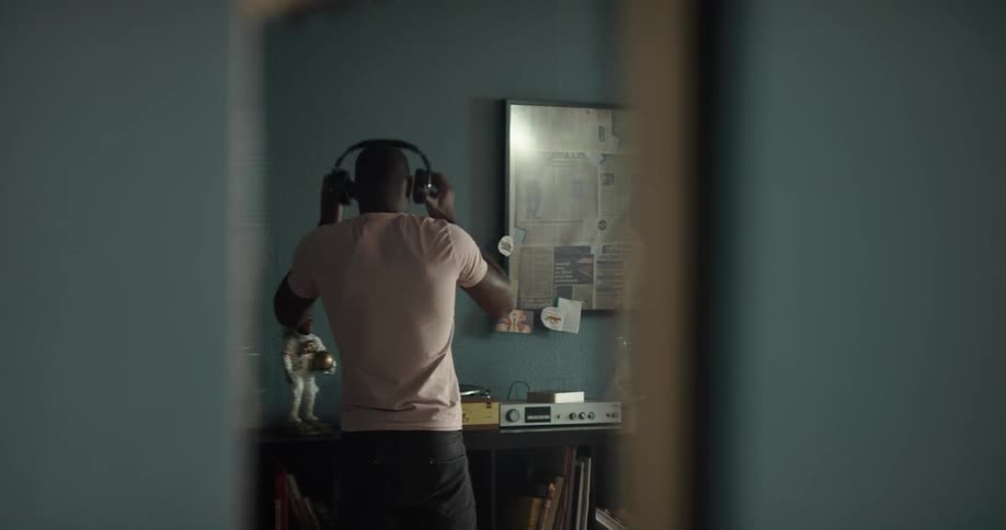 Mirror reflection of a black man putting on a headphone and dancing to the music from a vinyl record