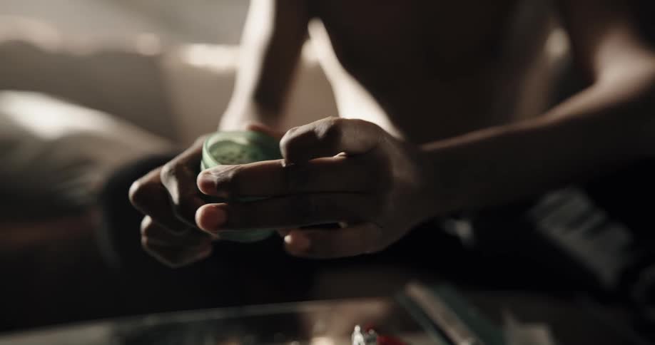 A man sitting at home puts a powdered substance in to a jar and puts a lid on and taps the jar