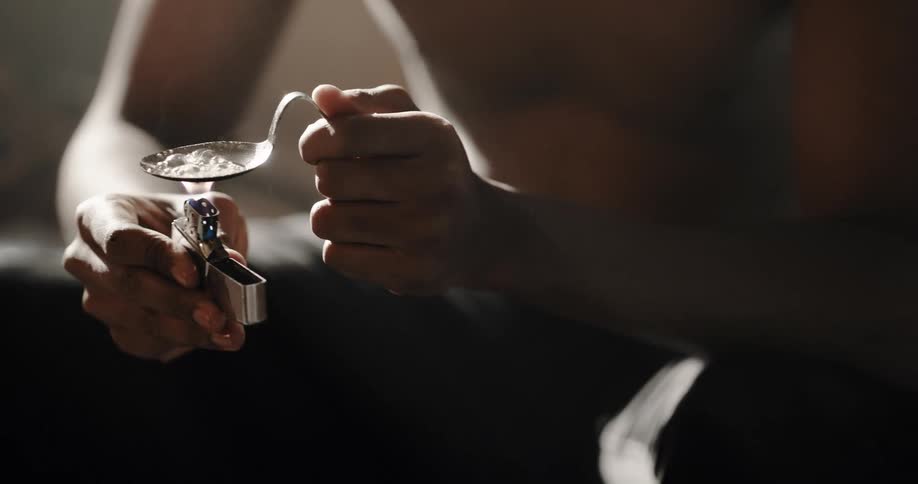 Man sitting on couch cooks substance in spoon with a lighter