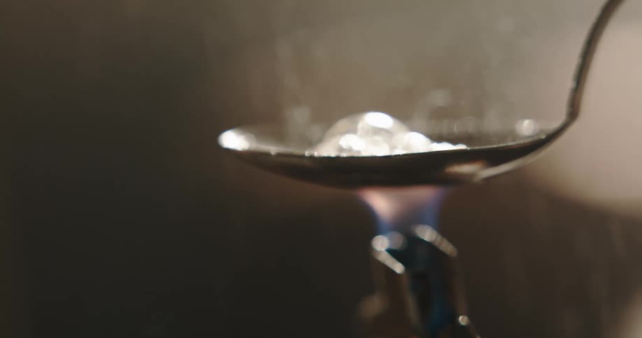 Man places a lighter under a spoon to cook drugs inside a dimly lit room at home