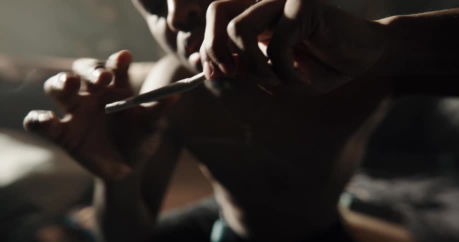 Shirtless man sitting on the couch in the living room rolling a joint