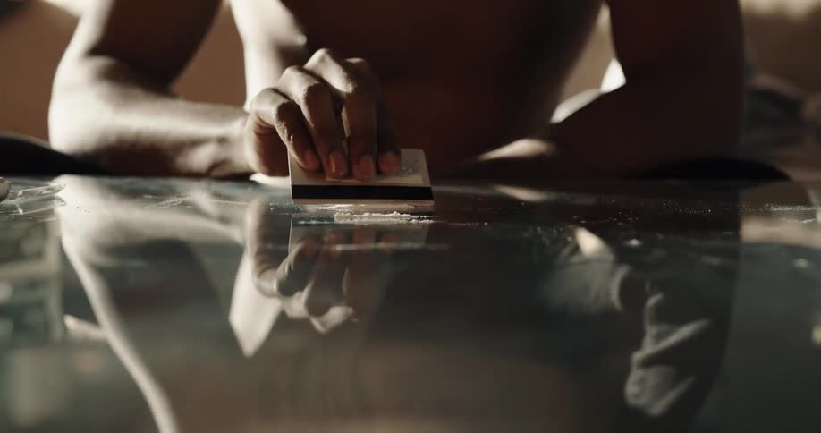 A man is using a credit card to make lines of cocaine on a table top