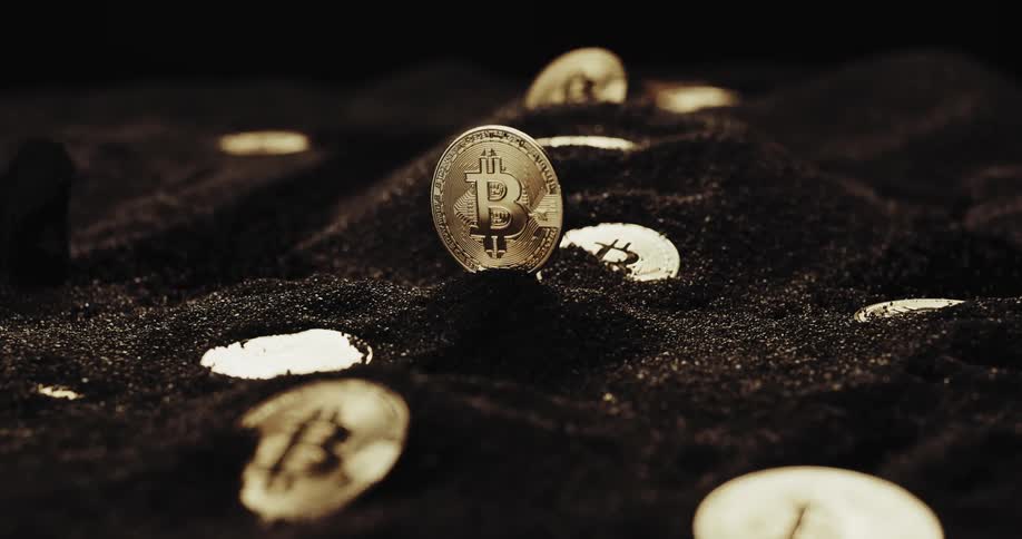 Close up of the shiny engraved surface of golden bitcoin physical coins resting on black sand