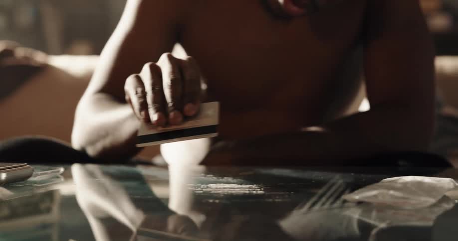 Man lines up illegal substance with a credit card sitting on couch