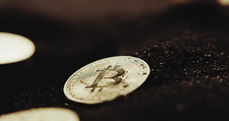Several coins with the bitcoin logo on them are atop a dark granular powder
