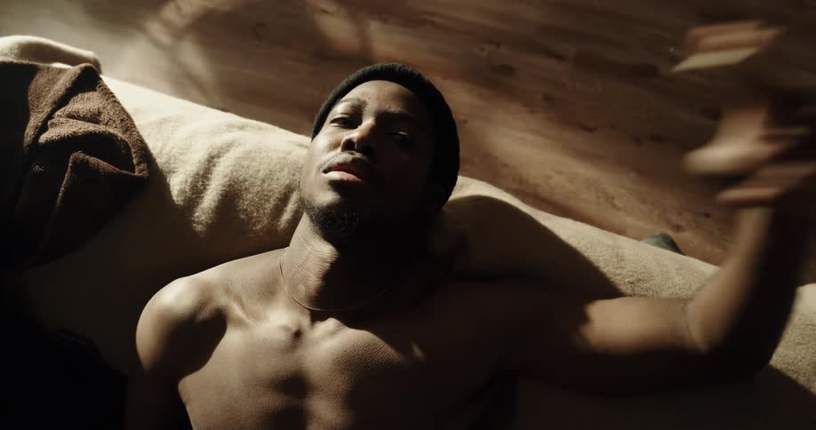 Shirtless black man sitting on the couch relaxing while smoking a cigarette