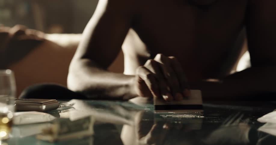 Drug addict arranging lines of coke with a credit card on a glass table