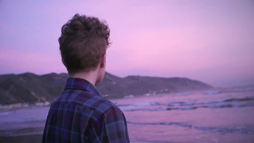 A woman stands by the water at sunset