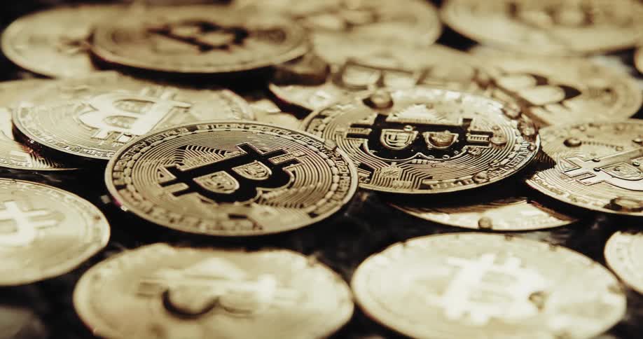 Close up of water running over the shiny engraved surface of golden bitcoin physical coins