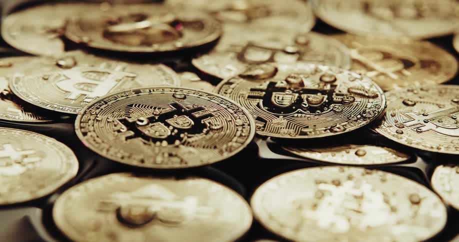 Close up of water running over the shiny engraved surface of golden bitcoin physical coins