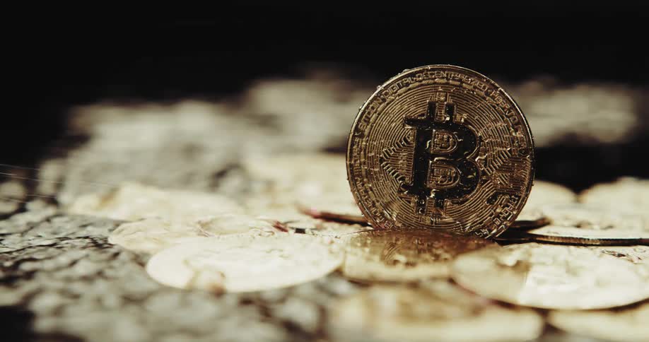 Water splashes near gold bitcoins and droplets roll off the coin