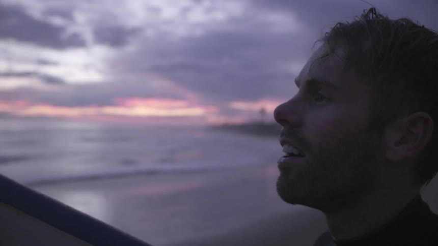 A man wipes his hair as he holds a surfboard