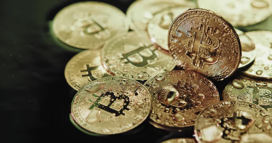 Golden coins with engraved bitcoin symbol sits in rippling water