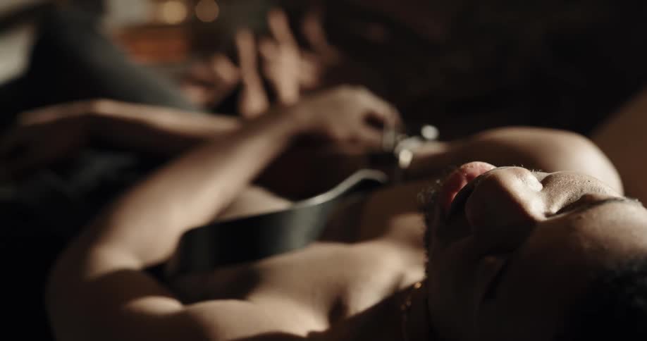 A shirtless young man sits unconscious with a belt wrapped around his arm
