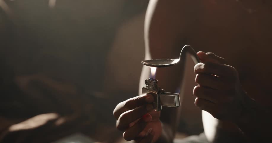Man sitting on a couch at home uses a syringe to fill a bent spoon to cook drugs
