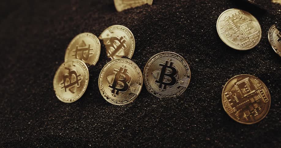 A studio shot of shiny bitcoins arranged in a mound of black sand
