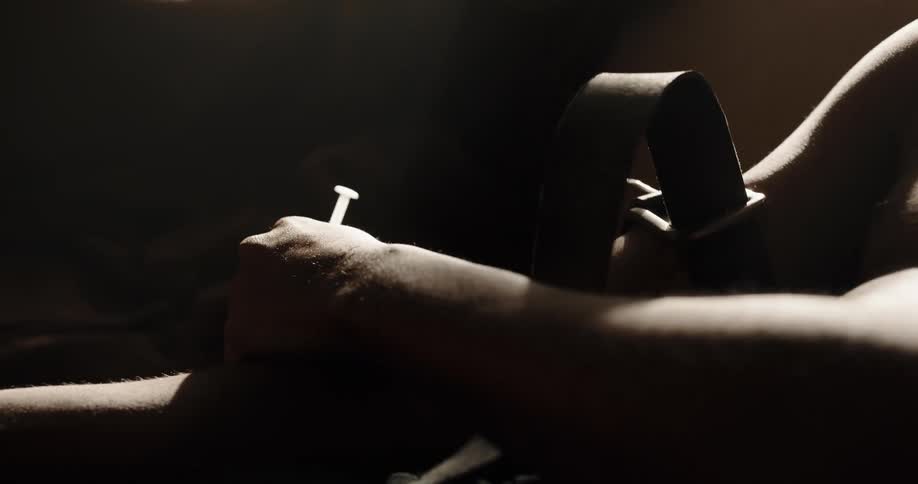 Black man high on drugs sitting on the couch and applying heroin on his arm with a syringe