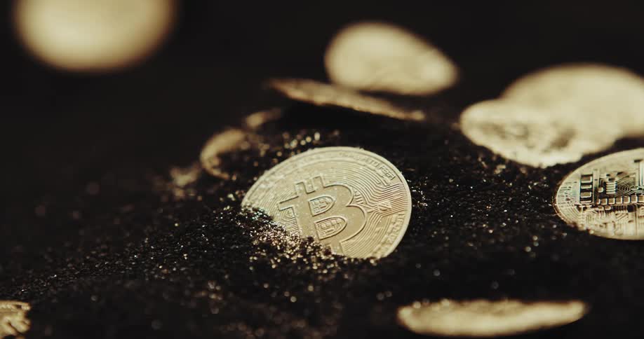 Wind blows particles of metal gold coins engraved with bitcoin symbol