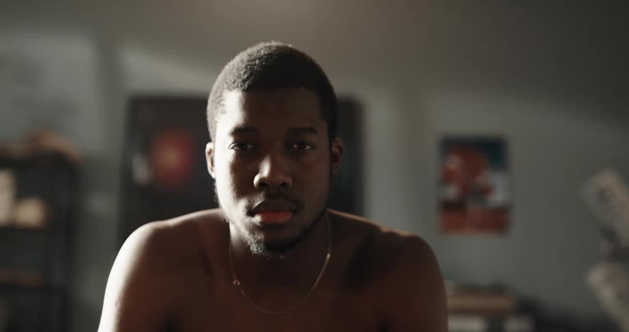Shirtless black man sitting on the couch of his house lifting his head up