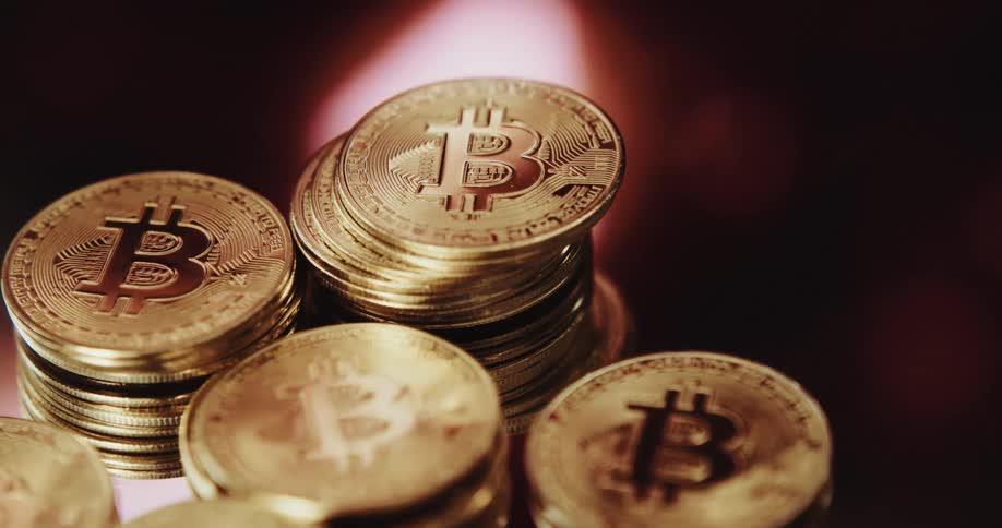 Close up of the shiny engraved surface of golden bitcoin physical coins over a reflecting surface